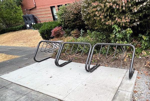 a bike rack in front of plants with a brick building