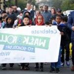 Students holding sign for walk and roll to school day with Superintendent Jones and Mayor Harrell