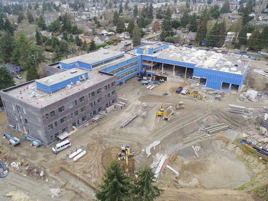 aerial of a large L-shaped building under construction with soil and equipment in between the wings