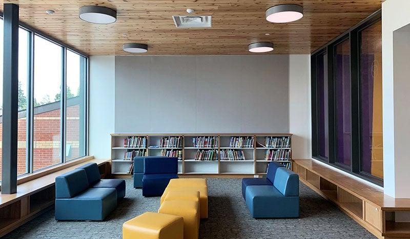 a group of low soft seating in a nook between two windows with a low bookshelf on the back wall