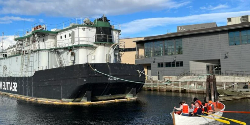 Students in rowboat next to large barge at Seattle Maritime Academy